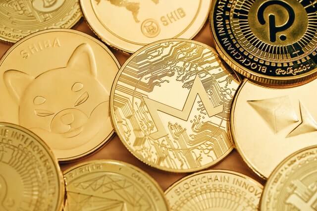 Various cryptocurrencies, including Monero, Shiba Inu, Ethereum, and Polkadot, represented by physical coins.