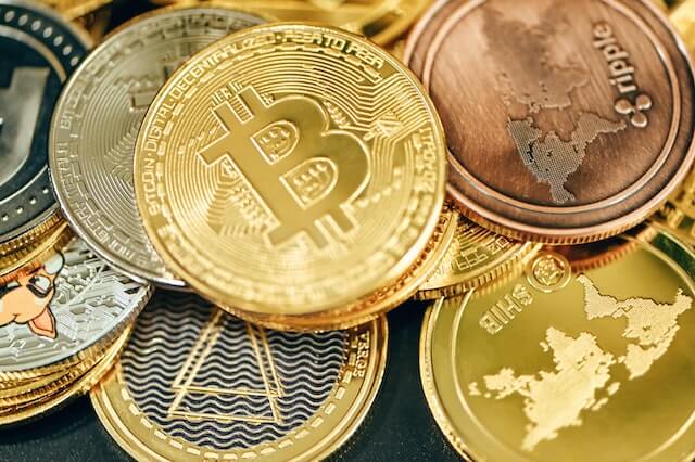 Various cryptocurrencies, including Bitcoin, Ripple, Shiba Inu, and more, represented by physical coins. 